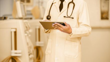 Arzt mit Tablet in der Hand steht vor Geräten zur Blutwäsche