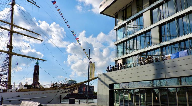 Kunden und Partner auf der Dachterrasse des Bürogebäudes bei der Parade der Deutschen Marine. Links der Hafen von Bremerhaven mit dem Schulschiff Deutschland im Vordergrund.