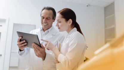 Eine Ärztin und ein Arzt schauen sich gut gelaunt medizinische Daten auf einem Tablet an